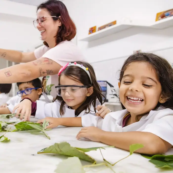 Menina sorrindo durante atividade com folhas na Educação Infantil